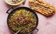 two pans filled with food on top of a pink tablecloth next to bread