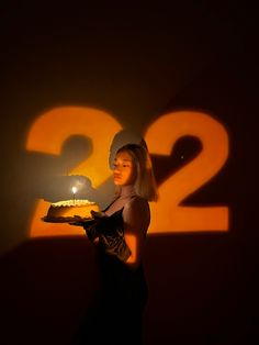 a woman holding a cake with the number twenty two on it in front of a dark background