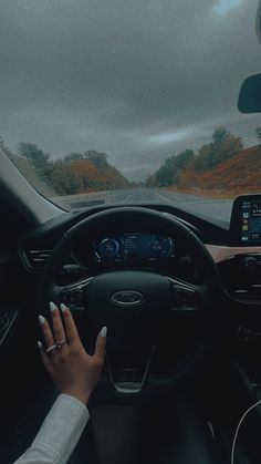 a woman driving a car on a road with her hands on the steering wheel and dashboard