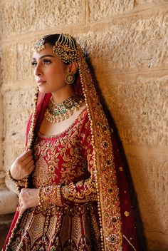 a woman in a red and gold bridal outfit leaning against a wall with her hands on her hips