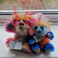 two colorful stuffed animals sitting next to each other in front of a window sill