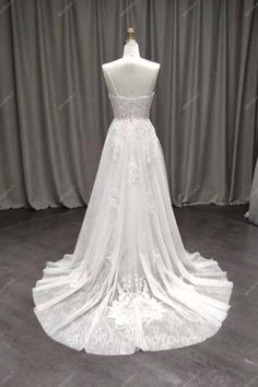 a white wedding dress on display in front of a gray backdrop with curtains behind it