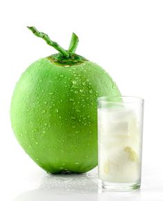 a green apple next to a glass of ice water on a white surface with drops of water