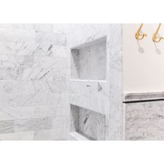 a bathroom with white marble walls and gold fixtures on the shower head, along with an open shelving unit