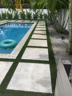 an empty swimming pool surrounded by palm trees and artificial grass in a tropical backyard area