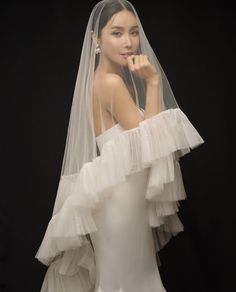 a woman wearing a white wedding dress with a veil on her head and one arm over her shoulder