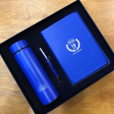 a blue notebook and pen in a black box on a wooden table with a medal