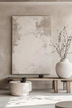 a white vase sitting on top of a wooden table next to a large piece of art