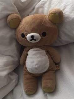 a brown teddy bear sitting on top of a bed next to white sheets and pillows