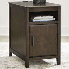 an end table with books and a remote control on top, in a living room