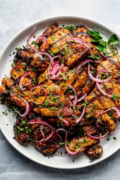 grilled chicken with onions and cilantro on a white platter, ready to be eaten