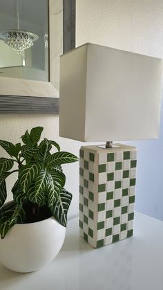 a white vase sitting next to a lamp on top of a table with a green plant in it