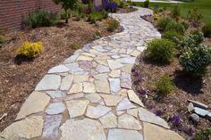 a stone path in front of a brick building with flowers and shrubs on the side