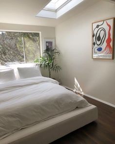 a white bed sitting in a bedroom next to a window with a potted plant on top of it