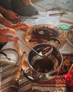 a woman is stirring chocolate into a pot with a ladle on the table in front of her