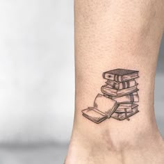 a black and white photo of a book tattoo on the ankle