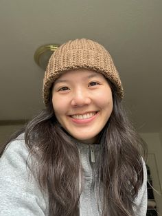 a woman with long hair wearing a knitted beanie smiles at the camera while standing in front of a door