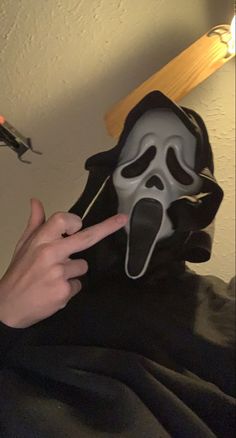 a person wearing a scream mask pointing at the camera with their finger in front of them