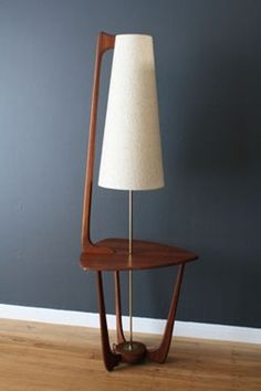 a lamp sitting on top of a wooden stand next to a wall with a white shade