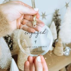 someone holding up a glass ornament with the word engaged on it