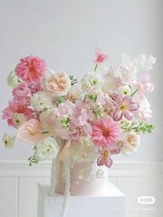 a white vase filled with lots of pink and white flowers on top of a table