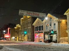 a city street with snow on the ground and buildings covered in christmas lights at night