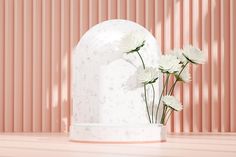 three white flowers are placed in front of a marble vase on a pink surface with vertical stripes