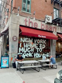 two men sitting on benches in front of a building with graffiti written on the side