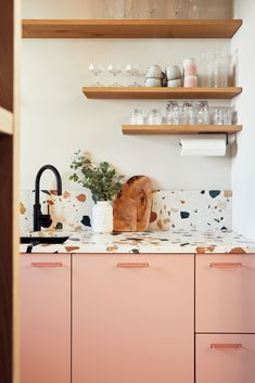 a kitchen with pink cupboards and shelves filled with dishes, cups and utensils