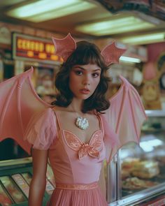 a woman in a pink dress with wings on her head standing next to a display case