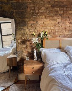 a bedroom with brick walls and white bedding, two nightstands and a mirror on the wall