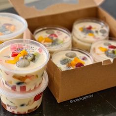 four desserts in plastic cups sitting on a table next to a cardboard box with the lid open