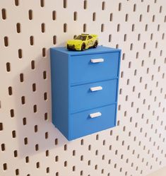 a toy car is sitting on top of a blue file cabinet against a white perfored wall