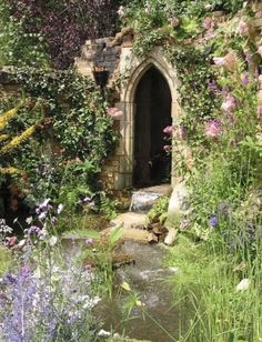 a garden with lots of flowers and plants around the entrance to an old stone building