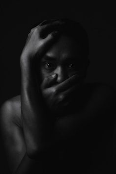 a black and white photo of a man with his hands on his face in the dark