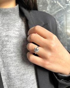 a woman's hand with a diamond ring on her finger, wearing a gray sweater