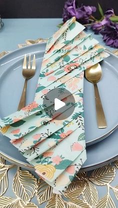 a blue plate topped with silverware next to a purple flowered table cloth and napkins