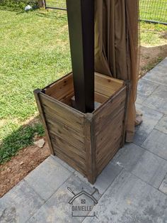 a wooden box sitting on top of a sidewalk next to a metal pole and fence