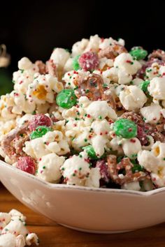 a bowl filled with white chocolate popcorn and sprinkles on top of a wooden table