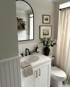 a white toilet sitting next to a sink in a bathroom under a mirror and framed pictures on the wall