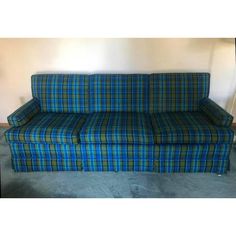 a blue and green plaid couch sitting on top of a carpeted floor next to a wall