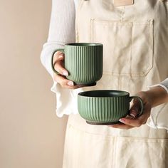 a woman holding two green mugs in one hand and an apron on the other