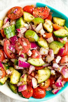 a colorful salad with cucumbers, tomatoes and onions in a blue bowl on a white cloth