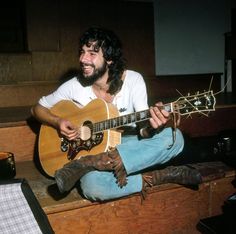 a man with long hair playing an acoustic guitar