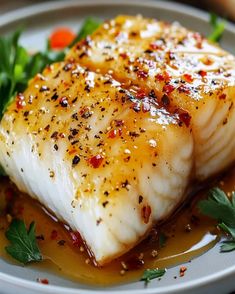 two fish fillets on a white plate with sauce and garnishes around them