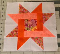 an orange and white star quilted on top of a table next to a ruler