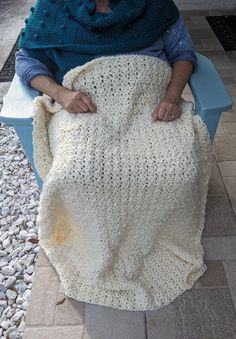 a woman is sitting on a bench with a crocheted blanket