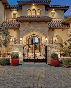 the entrance to a large home with two red planters on each side and an iron gate