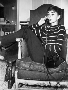 a woman sitting in a chair while talking on a cell phone and holding a camera