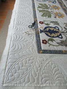 an embroidered table runner on top of a white bed sheet with blue and yellow flowers